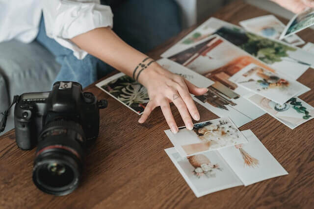 woman's hand sorting through photos on a table next to a black camera