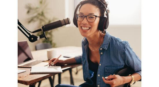 Woman podcaster smiling wearing headphones with mircophone on desk